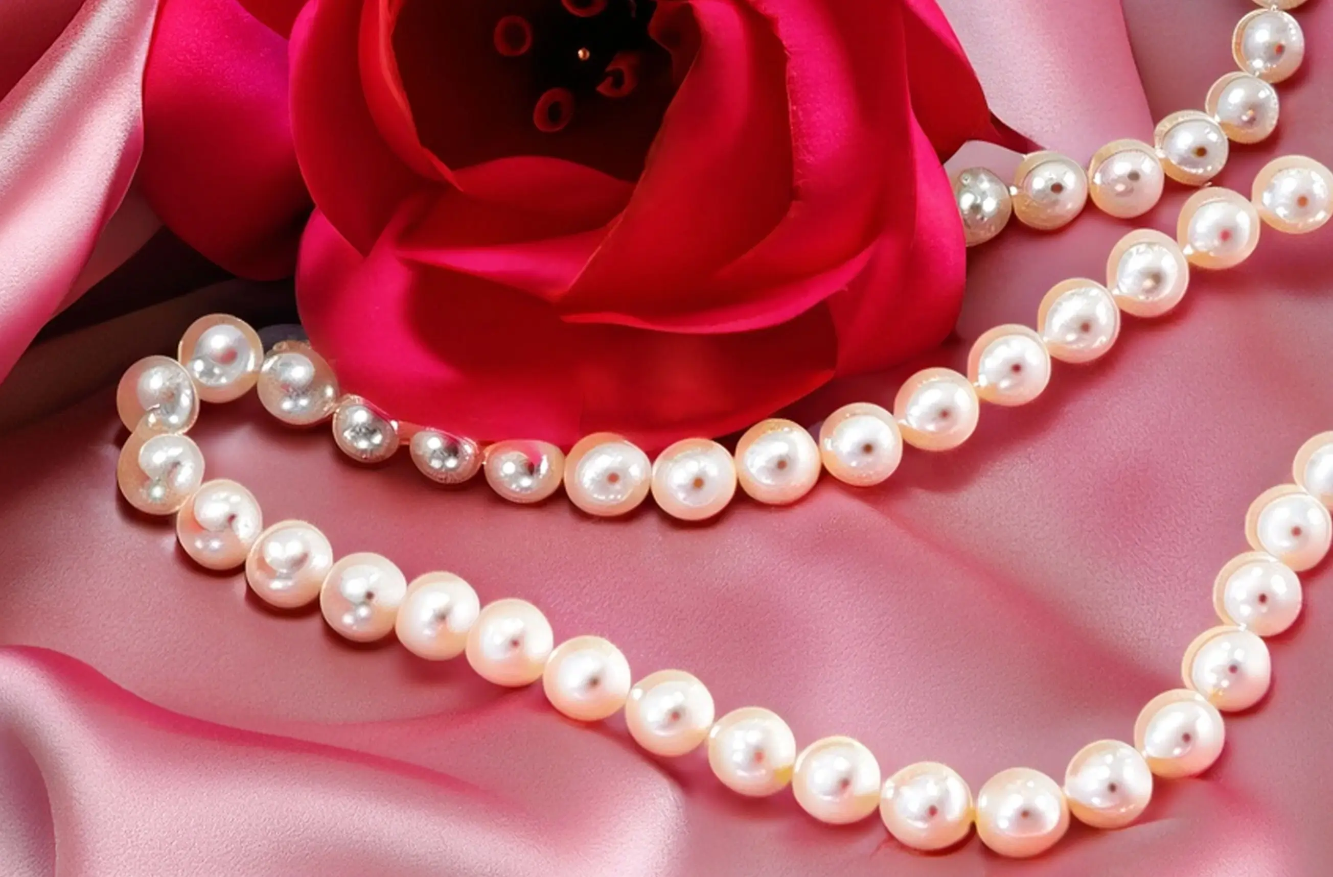 Elegant arrangement of a bright pink rose on satin with a classic pearl necklace, symbolizing luxury, traditional femininity, and the high-value woman advantage in securing a committed relationship.