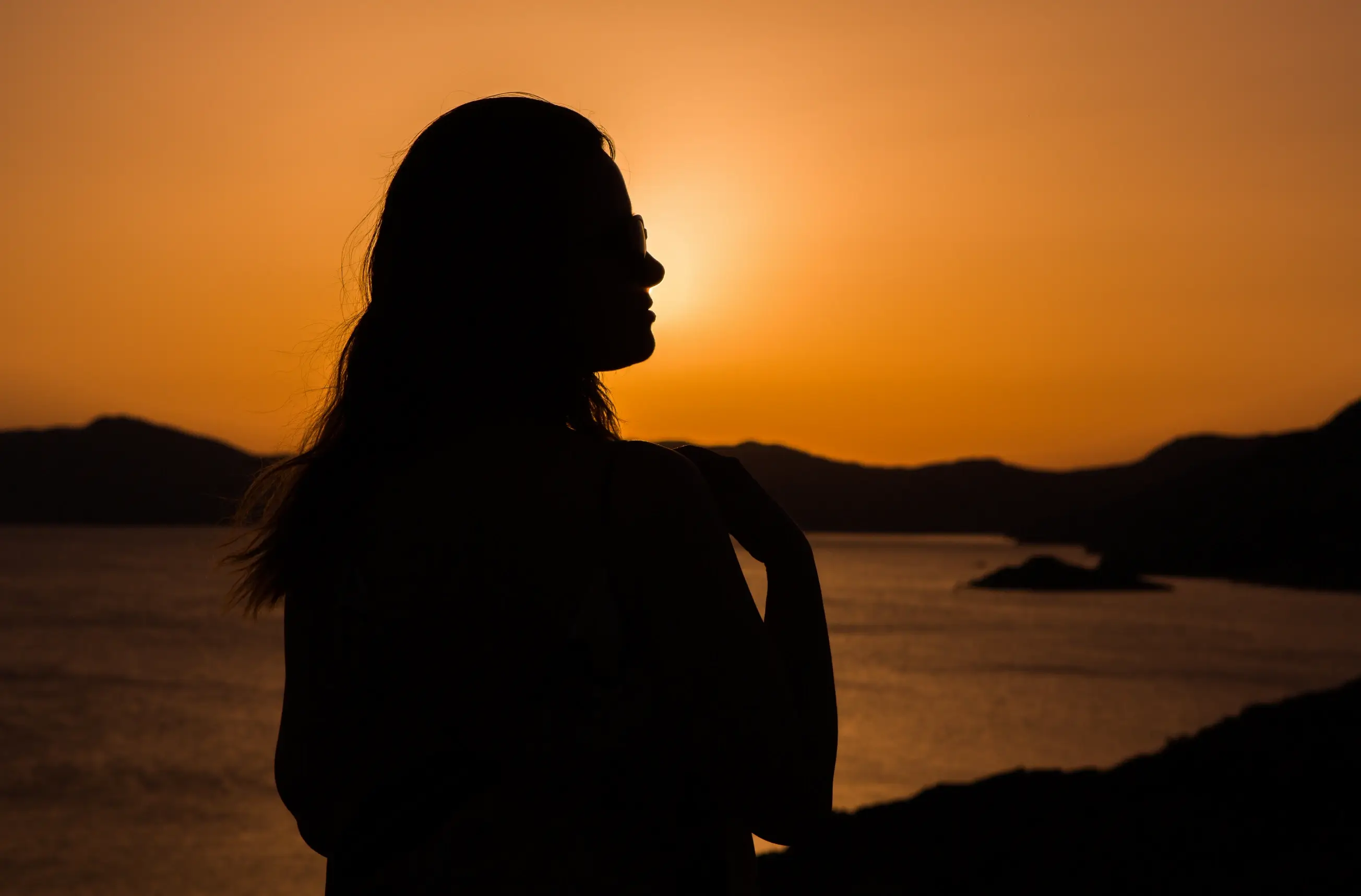 Silhouette of a mature woman standing against a golden sunset over the ocean, symbolizing female empowerment and the journey to finding true, mature love and quality relationships as a high-value woman.